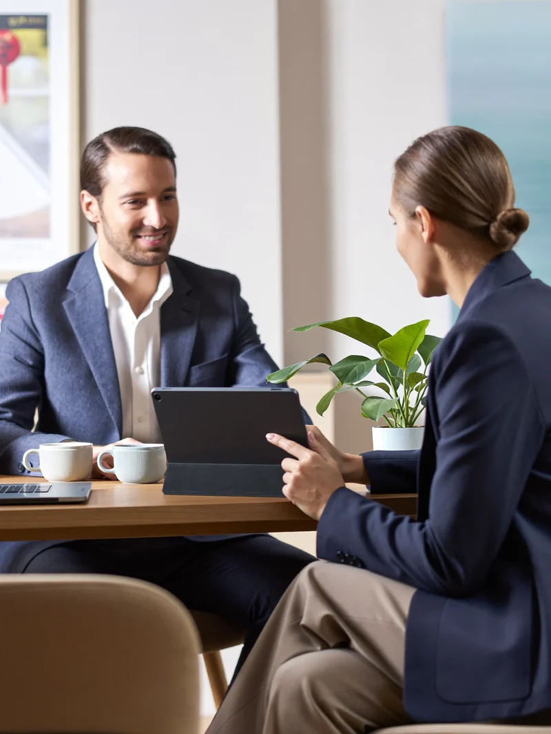 Freundliches Beratungsgespräch am Tisch mit Tablet, Kaffee und Pflanze